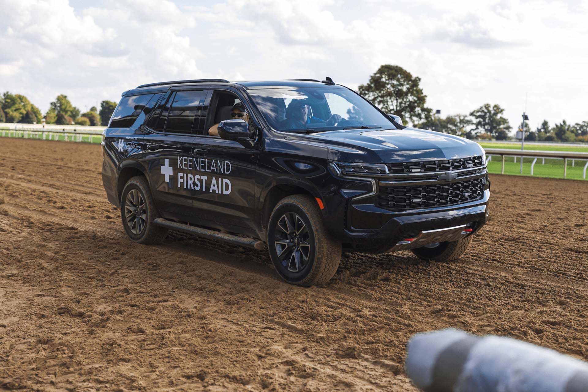 A picture of the Keeneland First Aid car on the dirt track. It is a large black Chevy SUV.